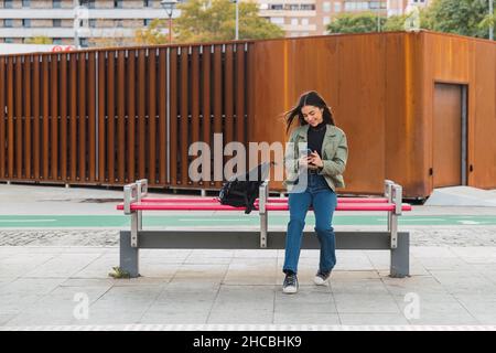 Frau, die auf der Bahnsteigbank ein Mobiltelefon benutzt Stockfoto