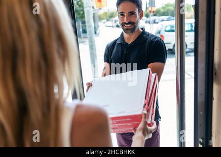 Lächelnder Liefermann, der der Geschäftsfrau vor der Tür Pizzakisten gab Stockfoto