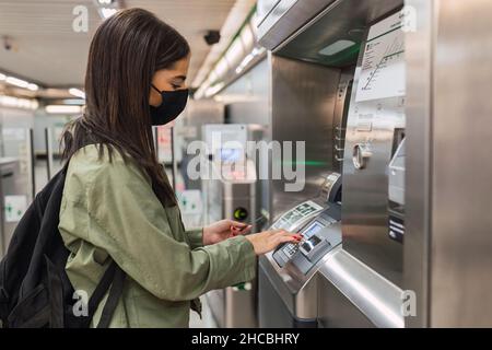 Junge Frau trägt Gesichtsmaske mit Ticket-Maschine Stockfoto