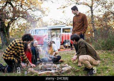 Fröhliche Freunde kochen Würste im Herbstwald auf Picknick Stockfoto