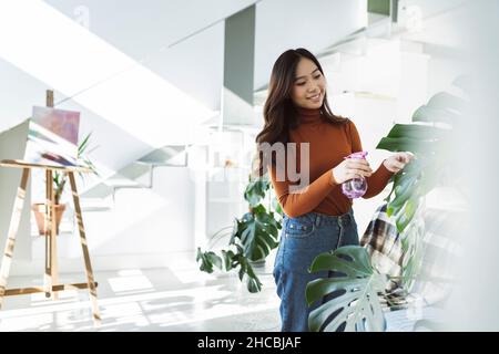Frau, die zu Hause Wasser auf die Topfpflanze sprüht Stockfoto