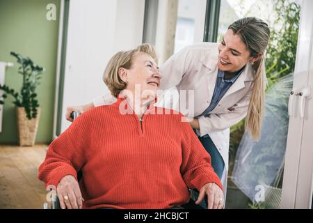 Behinderte Frau lächelt auf Krankenschwester, die hinter sich steht Stockfoto
