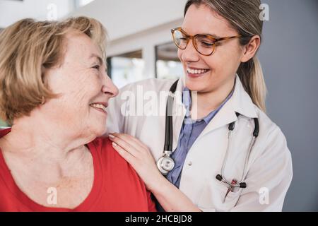 Lächelnder Arzt mit der Hand auf der Schulter des älteren Patienten zu Hause Stockfoto