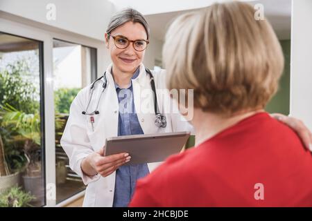 Junger Arzt mit der Hand auf der Schulter des Patienten zu Hause Stockfoto