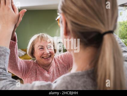 Ältere Frau, die zu Hause dem Pflegepersonal einen hohen Fünftel gibt Stockfoto