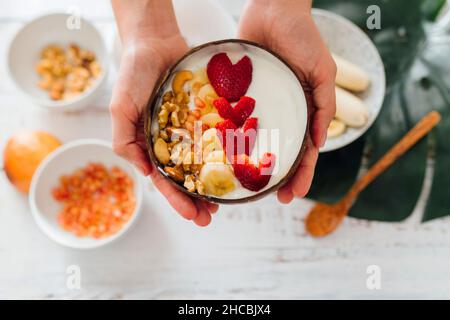 Frau hält eine Schüssel mit Joghurt und Früchten über den Tisch Stockfoto