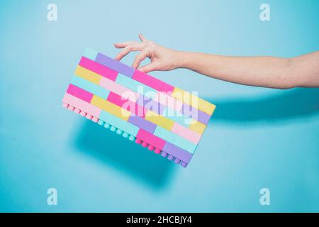 Arm der Frau mit bunten pastellfarbenen Spielzeugblöcken vor blauem Hintergrund Stockfoto