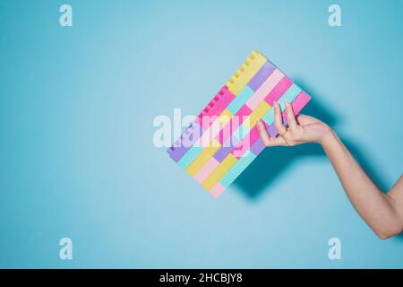 Arm der Frau mit bunten pastellfarbenen Spielzeugblöcken vor blauem Hintergrund Stockfoto