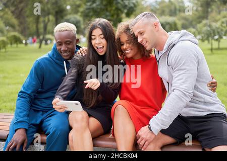 Multiethnische Freunde im Freien nehmen ein Selfie auf dem Smartphone. Diverse Gruppe Menschen Afro american Asian verbringen Zeit zusammen multirassischen männlichen weiblichen Studenten Sitzbank Park im Freien Stockfoto