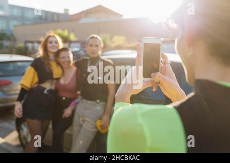 Mann, der Freunde am sonnigen Tag über das Mobiltelefon fotografiert Stockfoto