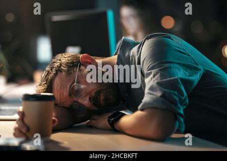 Überarbeiteter Geschäftsmann mit einem Einwegkaffee, der an der Rezeption im Büro nippte Stockfoto
