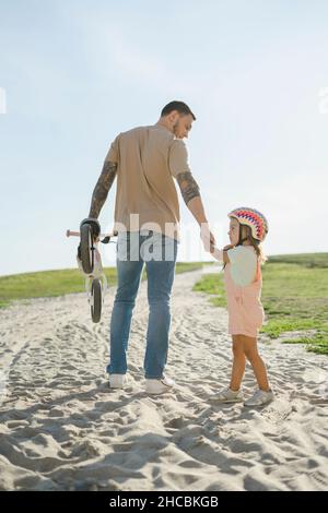 Vater mit Fahrrad, der auf dem Sand stehende Tochter ansieht Stockfoto