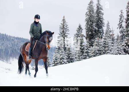 Junge Frau, die im Winter auf dem Pferd in den Bergen reitet Stockfoto