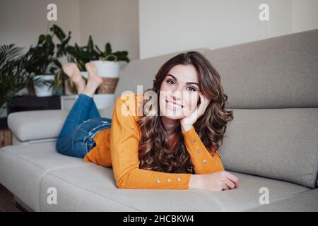 Schöne Frau mit welligen Haaren, die zu Hause auf dem Sofa liegt Stockfoto