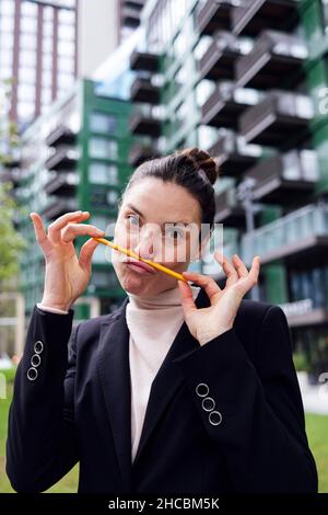 Geschäftsfrau, die im Büropark Schnurrbart mit Bleistift auf gepuckerten Lippen macht Stockfoto