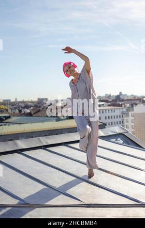 Verspielte Frau mit Kopfhörern, die auf dem Dach tanzen Stockfoto