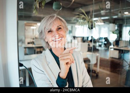 Lächelnde Geschäftsfrau mit Tablet-PC hinter Glasscheibe im Büro Stockfoto