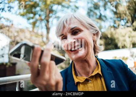 Lächelnde Geschäftsfrau, die Voicemail über das Mobiltelefon auf dem Dach sendet Stockfoto