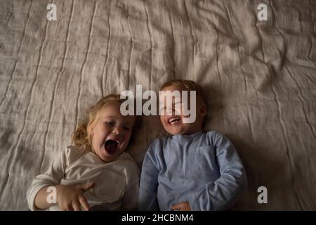 Unbeschwerte Zwillinge lachen zusammen und liegen zu Hause auf dem Bett Stockfoto