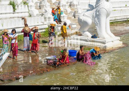 Menschen, die am Ufer des Irrawadden River baden und sich waschen, neben den Chinthe-Statuen, Burma Stockfoto