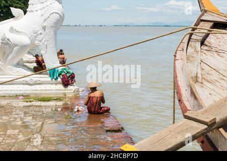 Menschen, die am Ufer des Irrawadden River baden und sich waschen, neben den Chinthe-Statuen, Burma Stockfoto