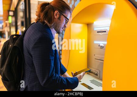 Geschäftsmann, der am U-Bahn-Ticketautomaten ein Mobiltelefon benutzt Stockfoto
