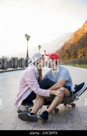 Ein romantisches Paar, das am Fußpfad auf dem Skateboard sitzt und sich die Nasen reibt Stockfoto