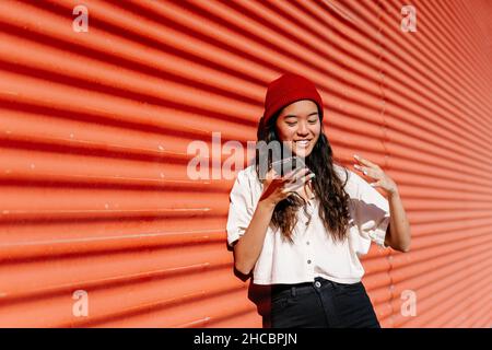 Frau, die Voicemail über das Mobiltelefon an der roten Wand sendet Stockfoto