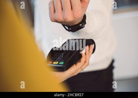 Mann, der über eine intelligente Uhr an die Kellnerin mit dem Kreditkartenleser im Café zahlte Stockfoto