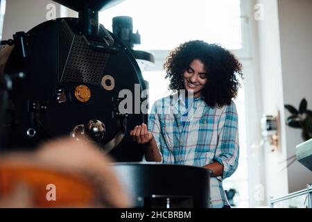 Lächelnder Besitzer, der in der Rösterei Kaffeebohnen in der Maschine röstet Stockfoto