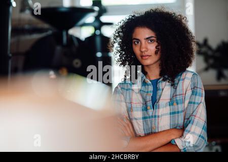 Seriöse Geschäftsfrau mit gekreuzten Armen bei der Kaffeerösterei Stockfoto