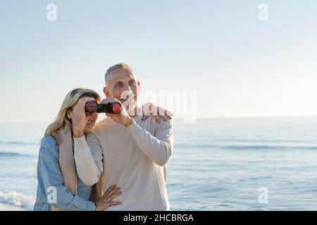 Frau schaute durch ein Fernglas, das von ihrem Mann am Strand gehalten wurde Stockfoto