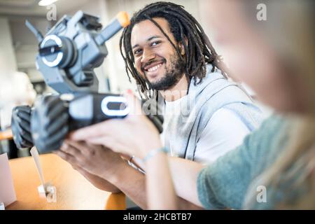 Junger Techniker schaut auf einen Ingenieur, der ein Roboterauto in der Werkstatt hält Stockfoto