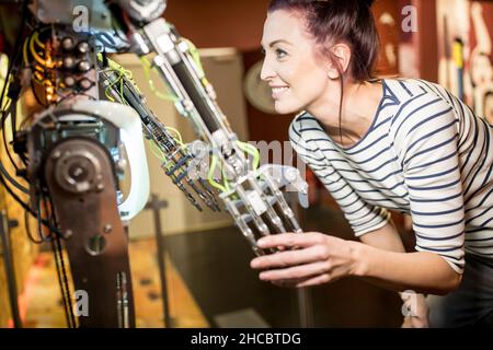 Lächelnder Techniker, der in der Werkstatt mit einem menschlichen Roboter die Hand schüttelt Stockfoto