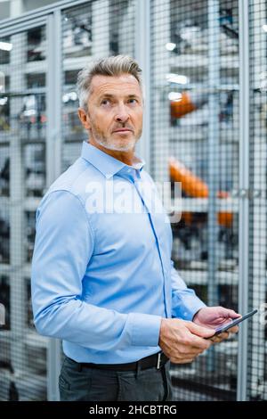 Ein nachdenklicher Geschäftsmann, der einen Tablet-PC im Werk hält Stockfoto