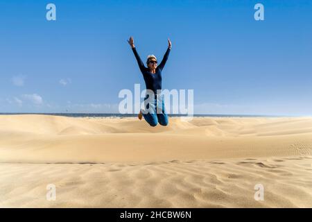 Glückliche Frau springt auf die Dünen im Maspalomas Nature Reserve, Gran Canaria, Kanarische Inseln, Spanien Stockfoto