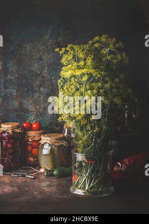 Dill Bunch Lagerung im Glas mit Wasser für die Konservierung am rustikalen Tisch mit verschiedenen Gläsern . Saisonale Zutaten zu Hause. Eingelegtes Gemüse. Vorderansicht. Stockfoto