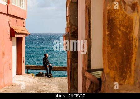 Ein Mann, der die Sonne und das Meer genießt, sitzt auf dem Geländer am Meer in Pozo Izquierdo, Gran Canaria, Kanarische Inseln, Spanien Stockfoto