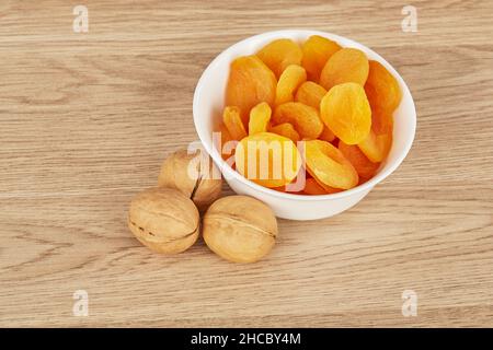 Weiße Schale mit getrockneten Aprikosen auf einem hölzernen Hintergrund mit drei Walnüssen Stockfoto