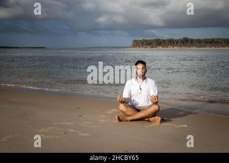 Weißer Mann zwischen 25 und 30 Jahren am Rande des Meeres beim Yoga. Meditation in der Natur. Stockfoto