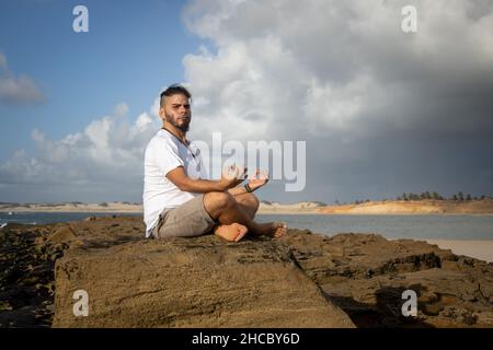 Weißer Mann zwischen 25 und 30 Jahren am Rande des Meeres beim Yoga. Meditation in der Natur. Stockfoto