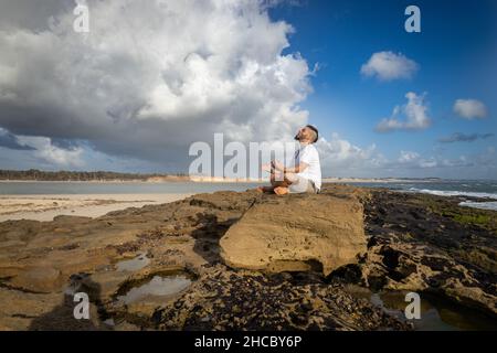 Weißer Mann zwischen 25 und 30 Jahren am Rande des Meeres beim Yoga. Meditation in der Natur. Stockfoto