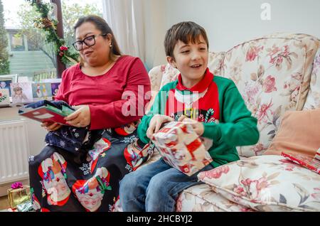 Mutter und Sohn saßen am Weihnachtstag auf einem Sofa und öffneten Geschenke Stockfoto