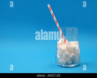 Glas mit Zuckerwürfeln und Papierstroh isoliert auf blauem Hintergrund mit Kopierraum Stockfoto