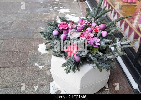 Weihnachtliche Blumenarrangements von trockenen Tannenzweigen, künstlichen Anemonen und Rosen in Himbeer- und Purpurtönen, bedeckt mit Schnee Stockfoto