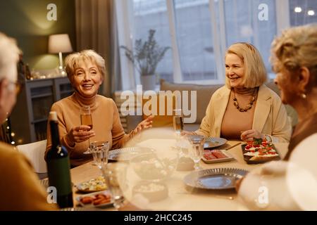 Eine Gruppe älterer Freunde traf sich am Esstisch und hatte ein festliches Abendessen. Schöne alte Frau, die Toast macht Stockfoto