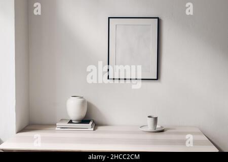 Elegantes, minimalistisches Home-Office – Standbild. Weiße Vase, Tasse Kaffee, Zeitschriften. Holztisch Hintergrund in Sonnenlicht. Leeres schwarzes Bild Stockfoto