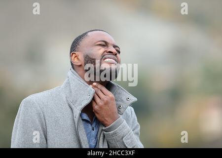 Kranker Mann mit schwarzer Haut, der im Winter unter Halsschmerzen leidet Stockfoto