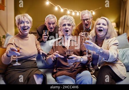 Eine Gruppe von fünf alten Freunden traf sich mit Wein- und Sektgläsern in den Händen um die Couch und schaute während des festlichen Abendessens auf die Kamera Stockfoto