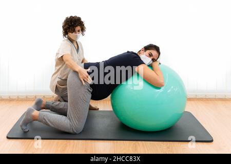 Eine Schwangerin macht Pilates-Übungen mit einem Ball mit Hilfe ihres Physiotherapeuten Stockfoto